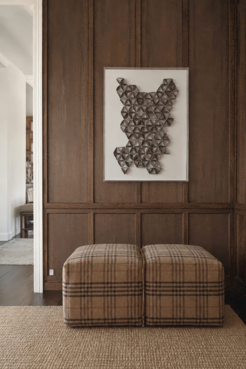 Cuadro de relieve geométrico gris sobre panel de madera en un recibidor